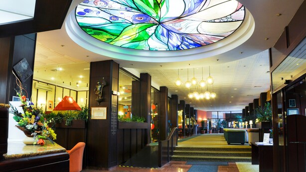 A hotel lobby with a large stained glass ceiling, a reception desk, and a staircase leading to upper floors. - Hotel Lövér Sopron (Sopron)