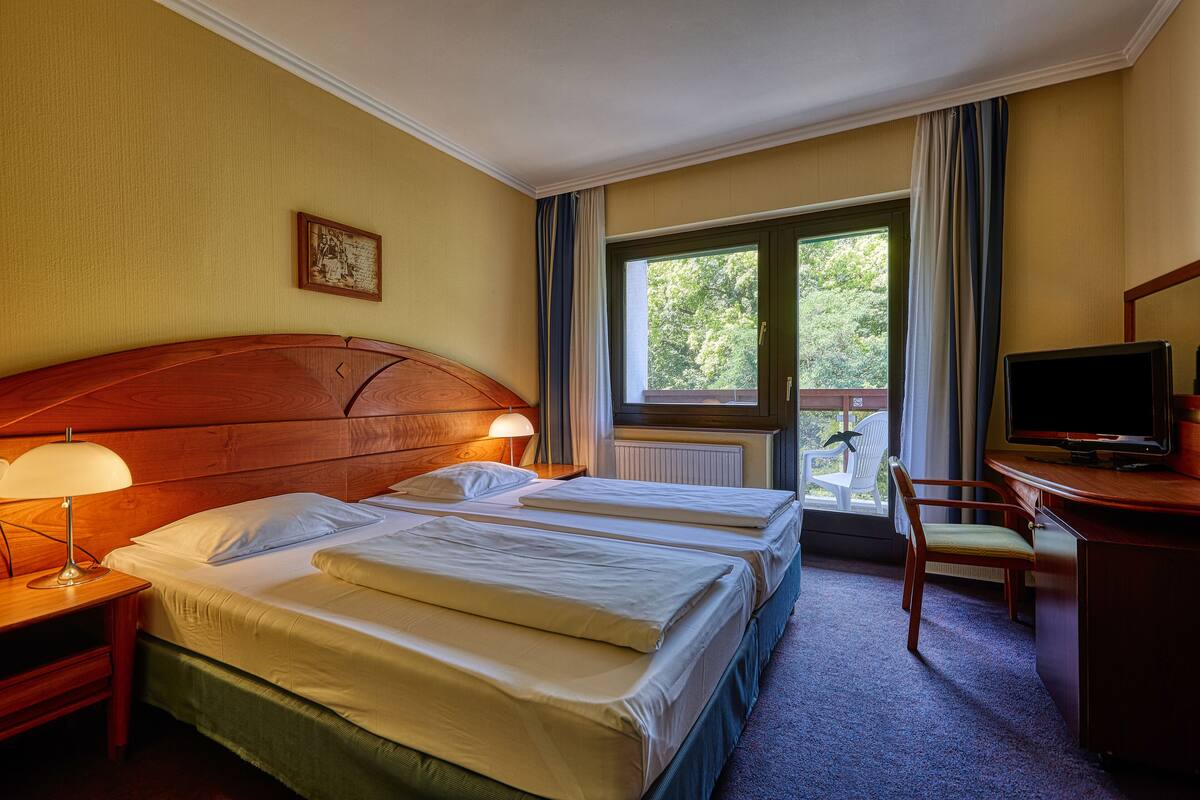 A hotel room with two beds, a desk with a TV, a chair, and a window with curtains.