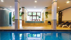 An indoor swimming pool with a tiled floor, a bench area with chairs, and a reception desk with a window view. - Hotel Lövér Sopron (Sopron)