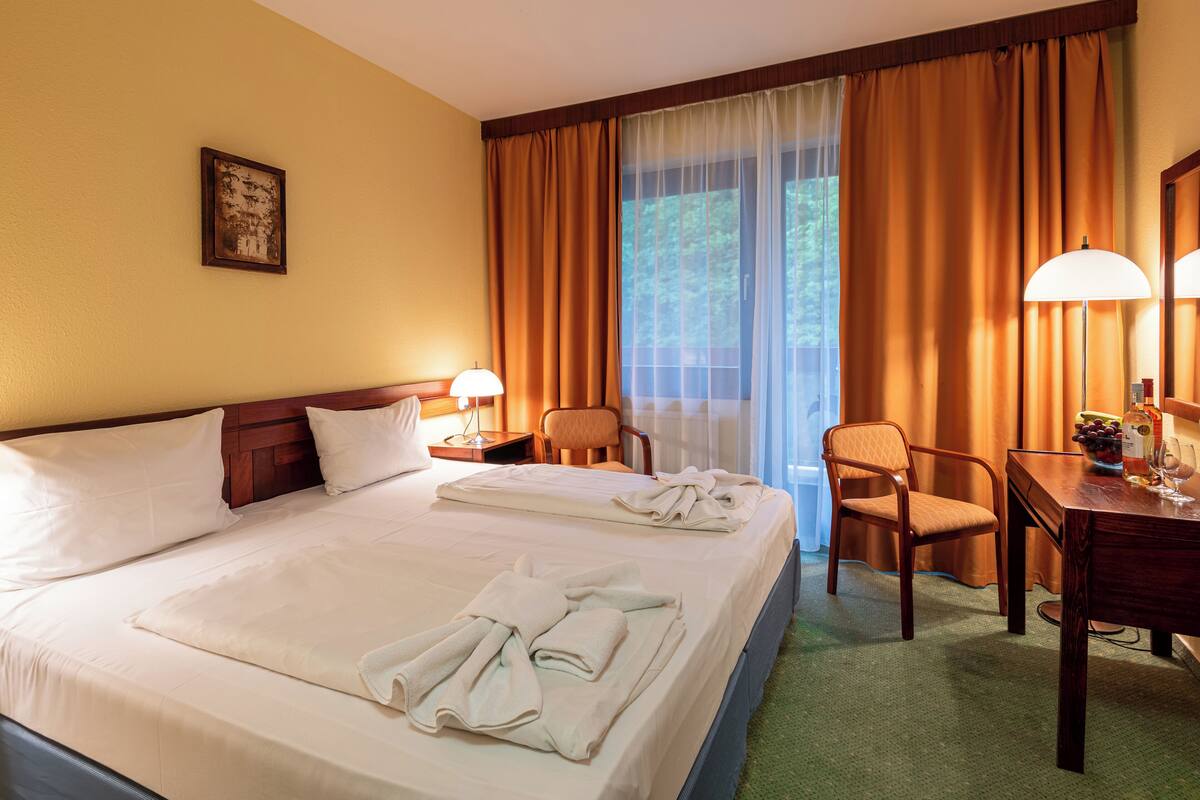 A hotel room with a large bed, two chairs, a desk, and a window with curtains.