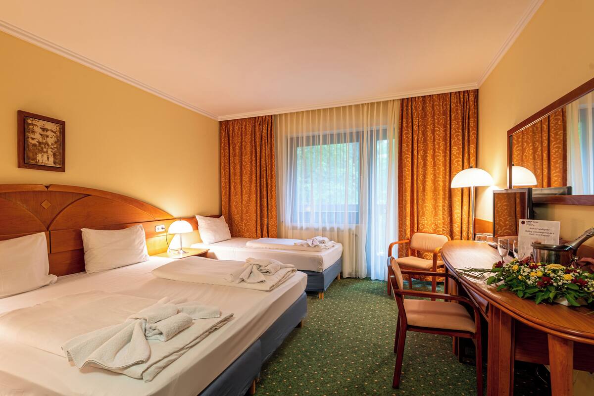 A hotel room with two beds, a desk with a chair, a lamp, and a mirror.