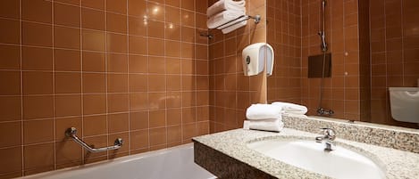 Ein Badezimmer mit einer weißen Badewanne, einem Waschtisch aus Granit, einem Handtuchhalter, einer Handbrause und einer Seifenspender.