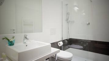Un baño moderno con lavamanos blanco, inodoro y ducha con mampara de vidrio.