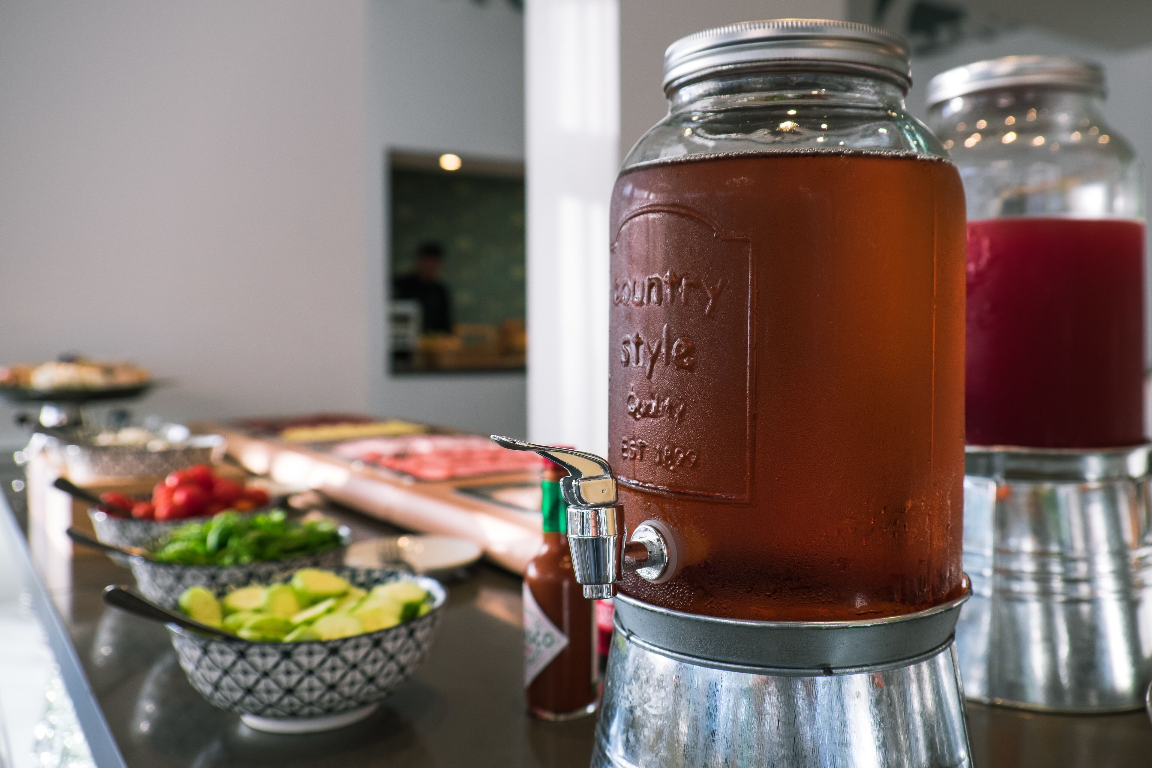 A kitchen counter with a large metal container labeled "country style" and a red beverage in a glass jar.