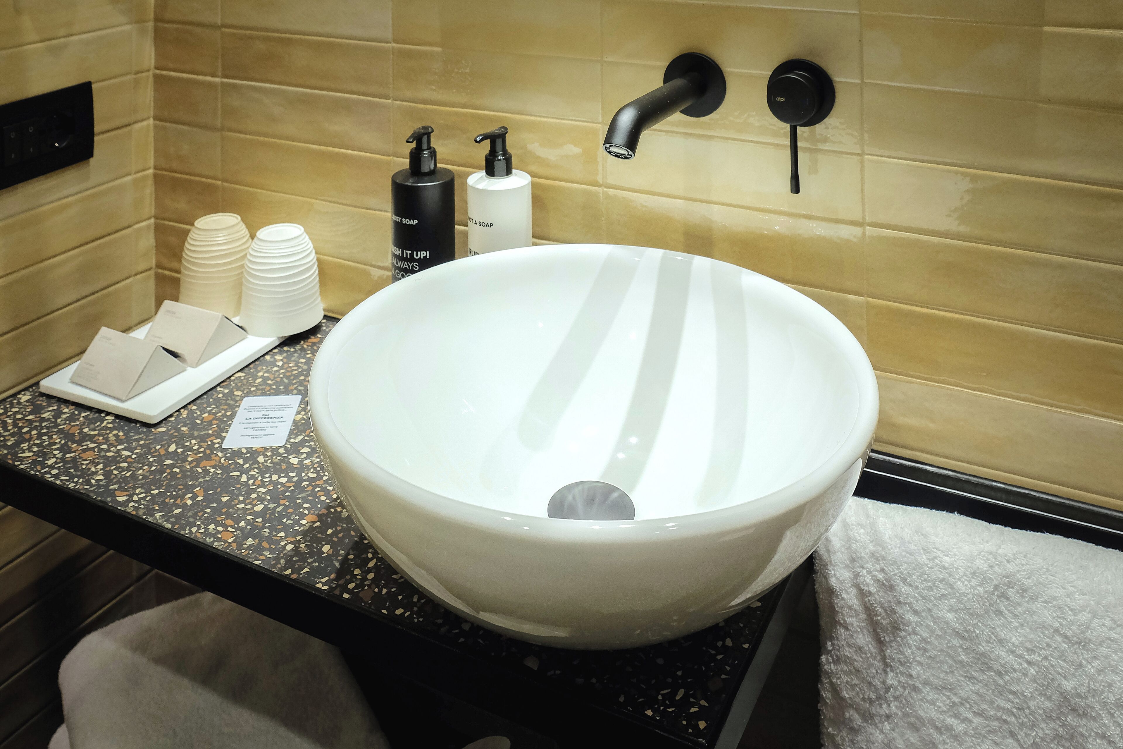 A bathroom with a large white sink, two black faucets, and toiletries on the counter.