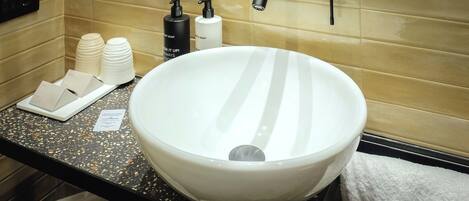 A bathroom with a large white sink, two black faucets, and toiletries on the counter.