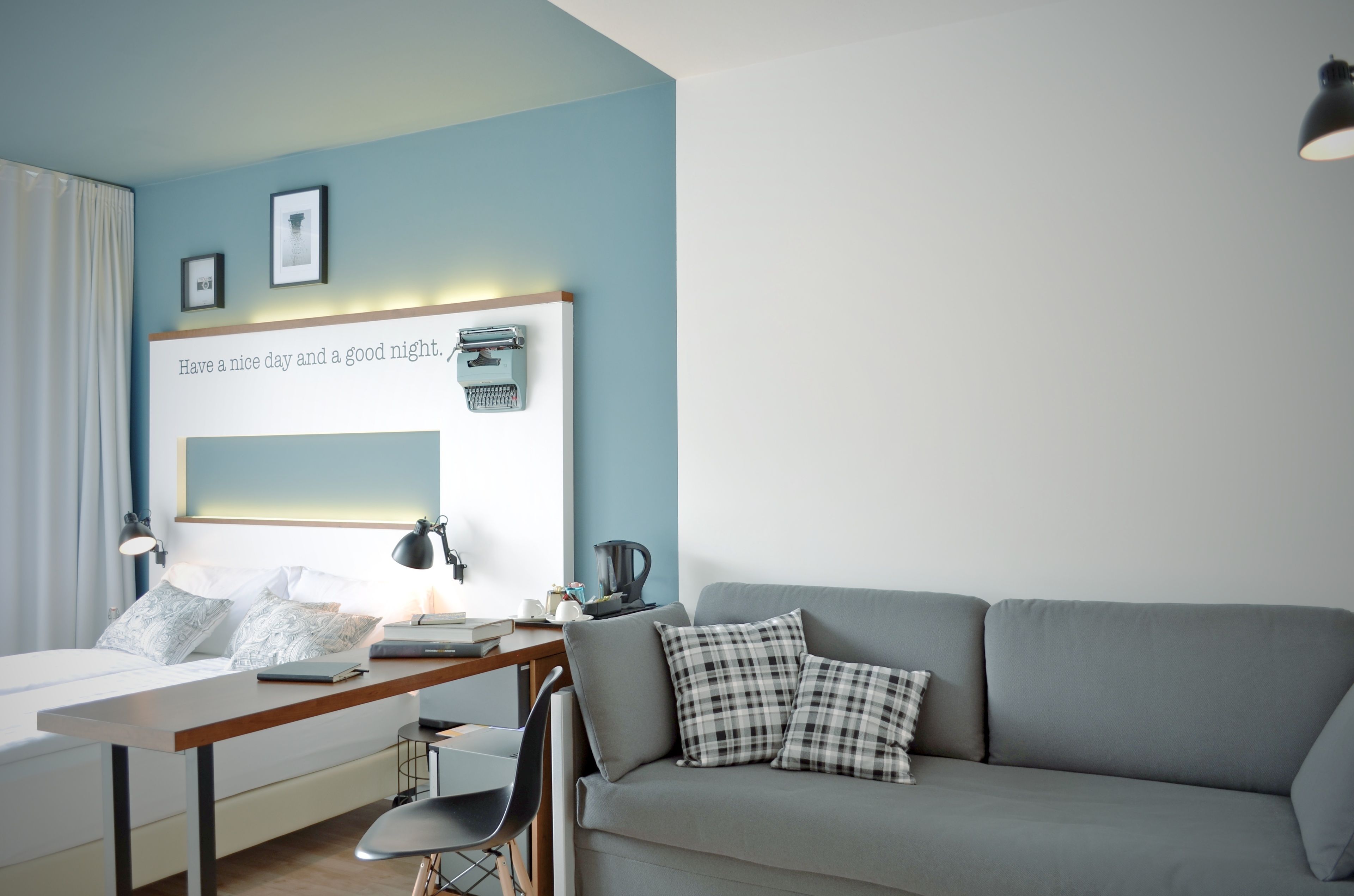 A modern bedroom with a bed, desk, and a grey sofa.