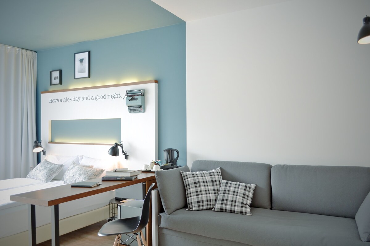 A modern bedroom with a bed, desk, and a grey sofa.
