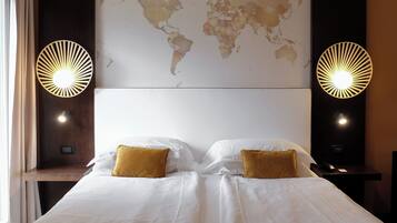 A hotel room with a large bed, two gold pillows, a world map on the wall, and two wall-mounted lights.