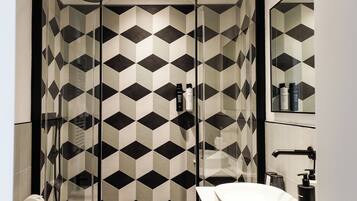 A modern bathroom with a geometric patterned shower enclosure, a white sink, and a mirror above the sink.