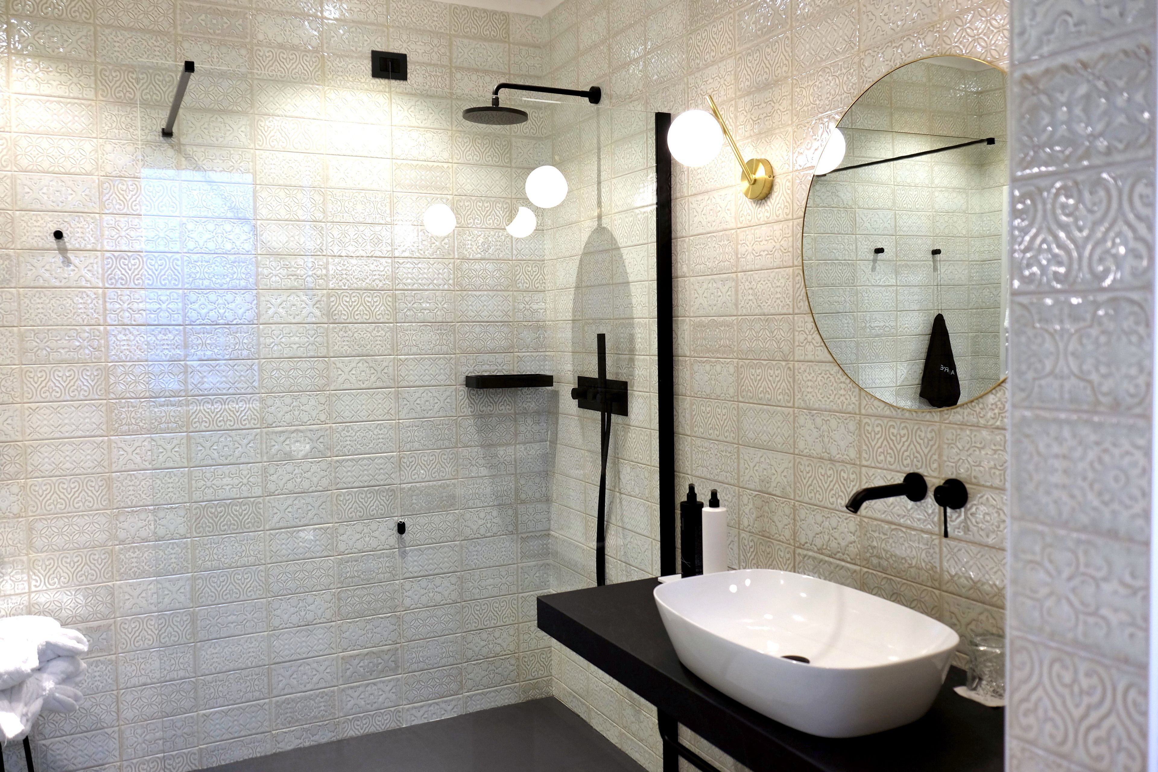 Un baño moderno con baldosas estampadas, un lavabo blanco, accesorios negros y un espejo grande.
