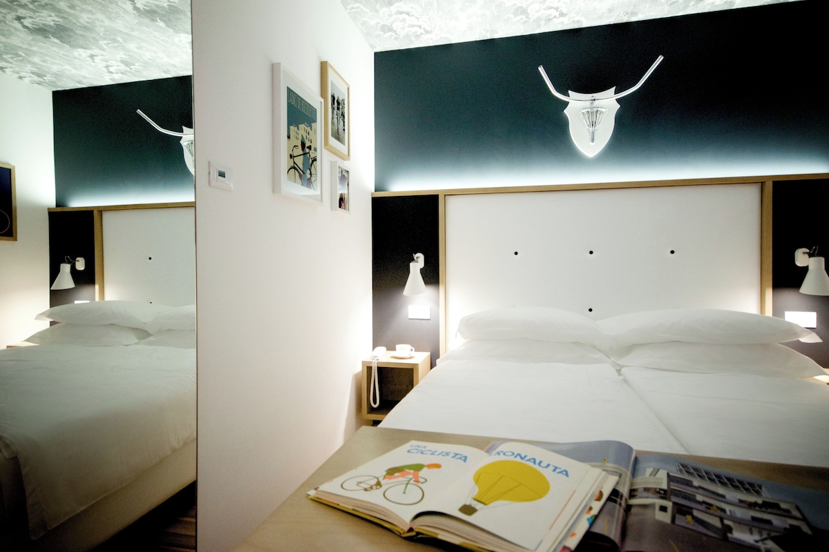 A hotel room with two beds, a nightstand with a lamp, and a ceiling with a light fixture.
