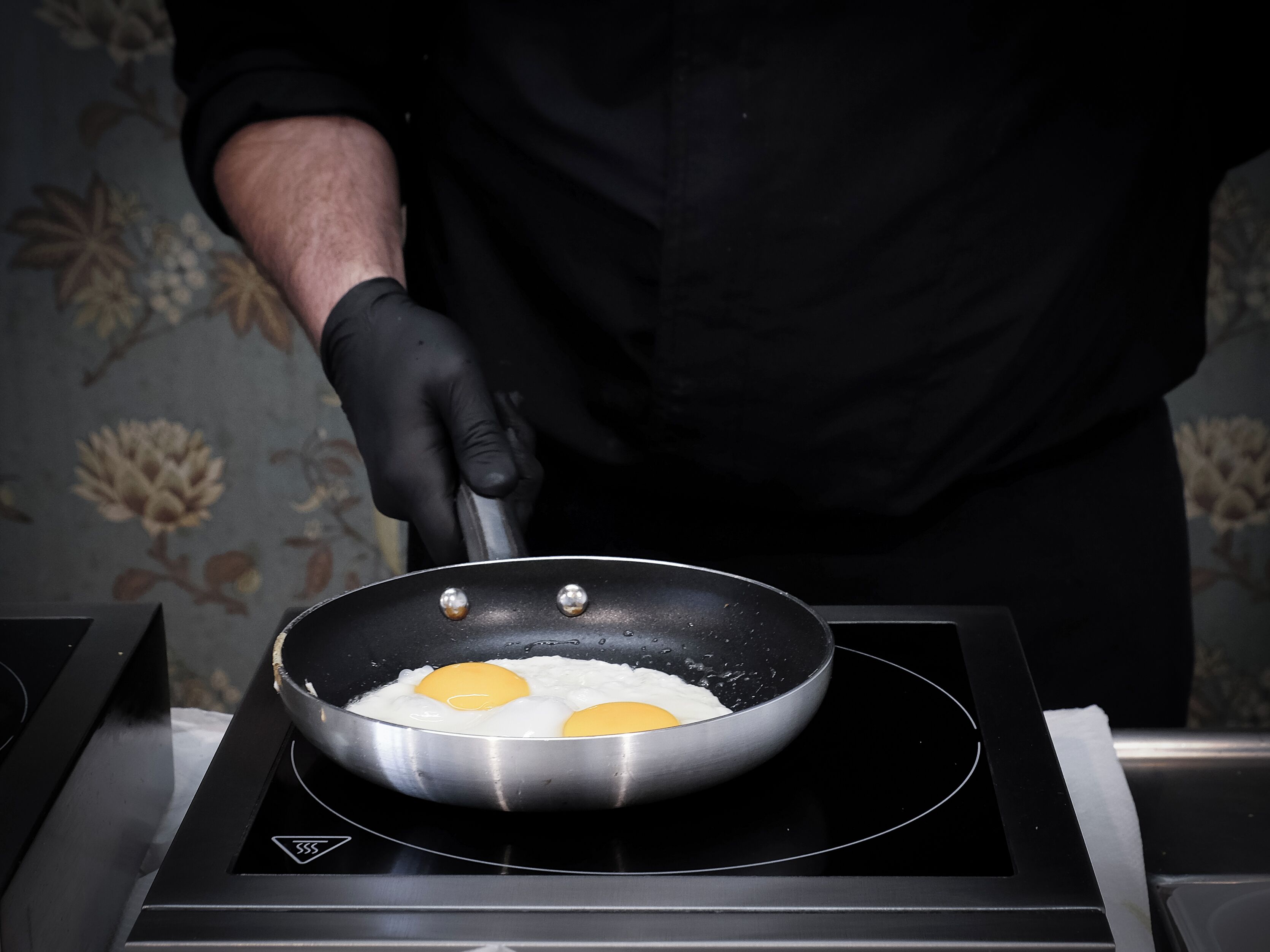 Una persona cocinando huevos en una sartén sobre una cocina por inducción.