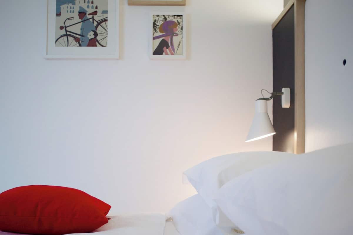 Una habitación de hotel con una cama, almohadones rojos y tres cuadros en la pared.