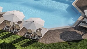 Vista aerea di una piscina con lettini e ombrelloni, circondata da una zona pavimentata e vegetazione.