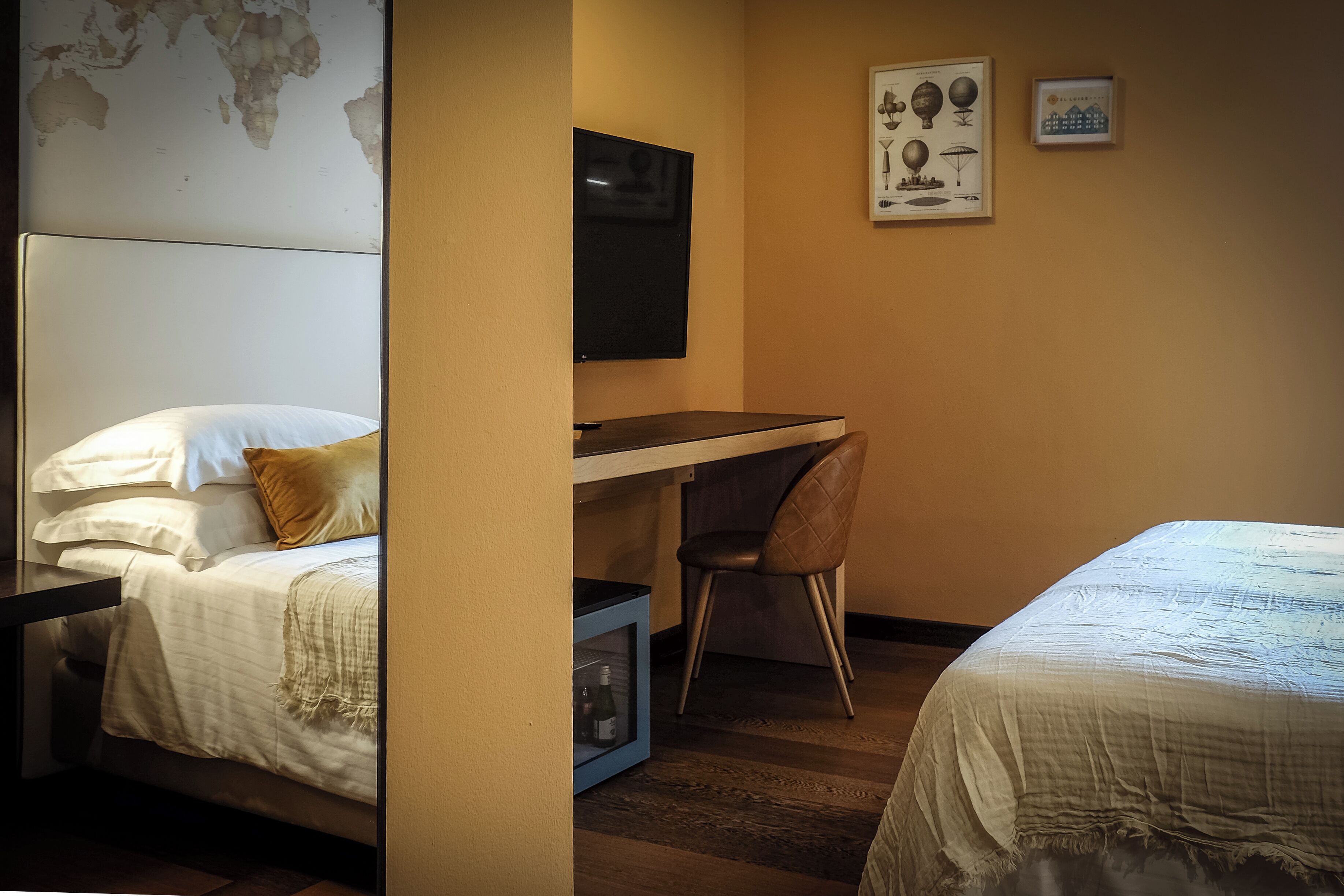 A hotel room with a bed, a desk, a chair, a TV, and a world map on the wall.
