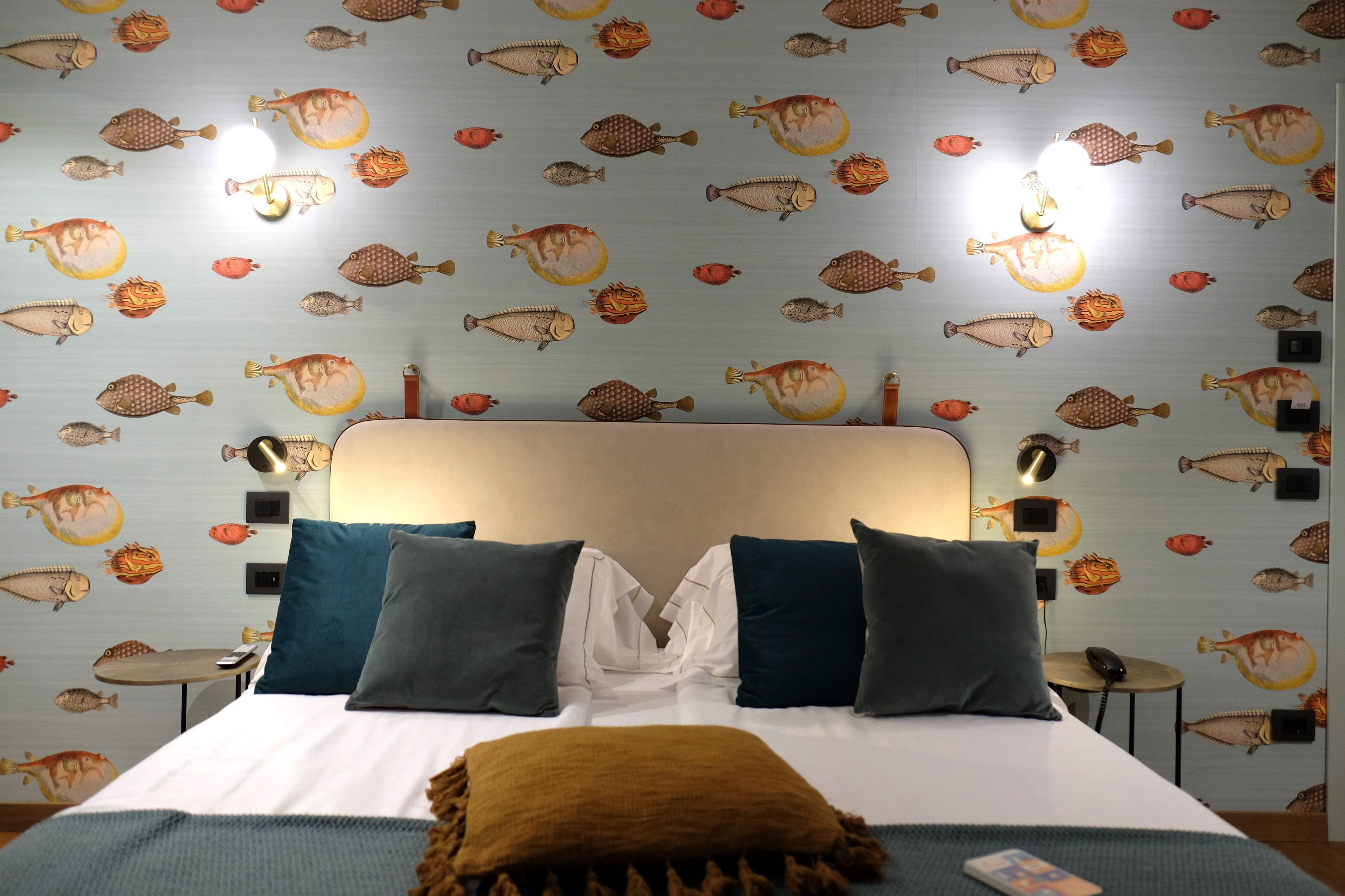 A hotel room with a bed, pillows, a bedside table, and a wall with fish decals.