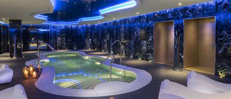 Un moderno espacio de spa con piscina climatizada, sillones blancos y velas.