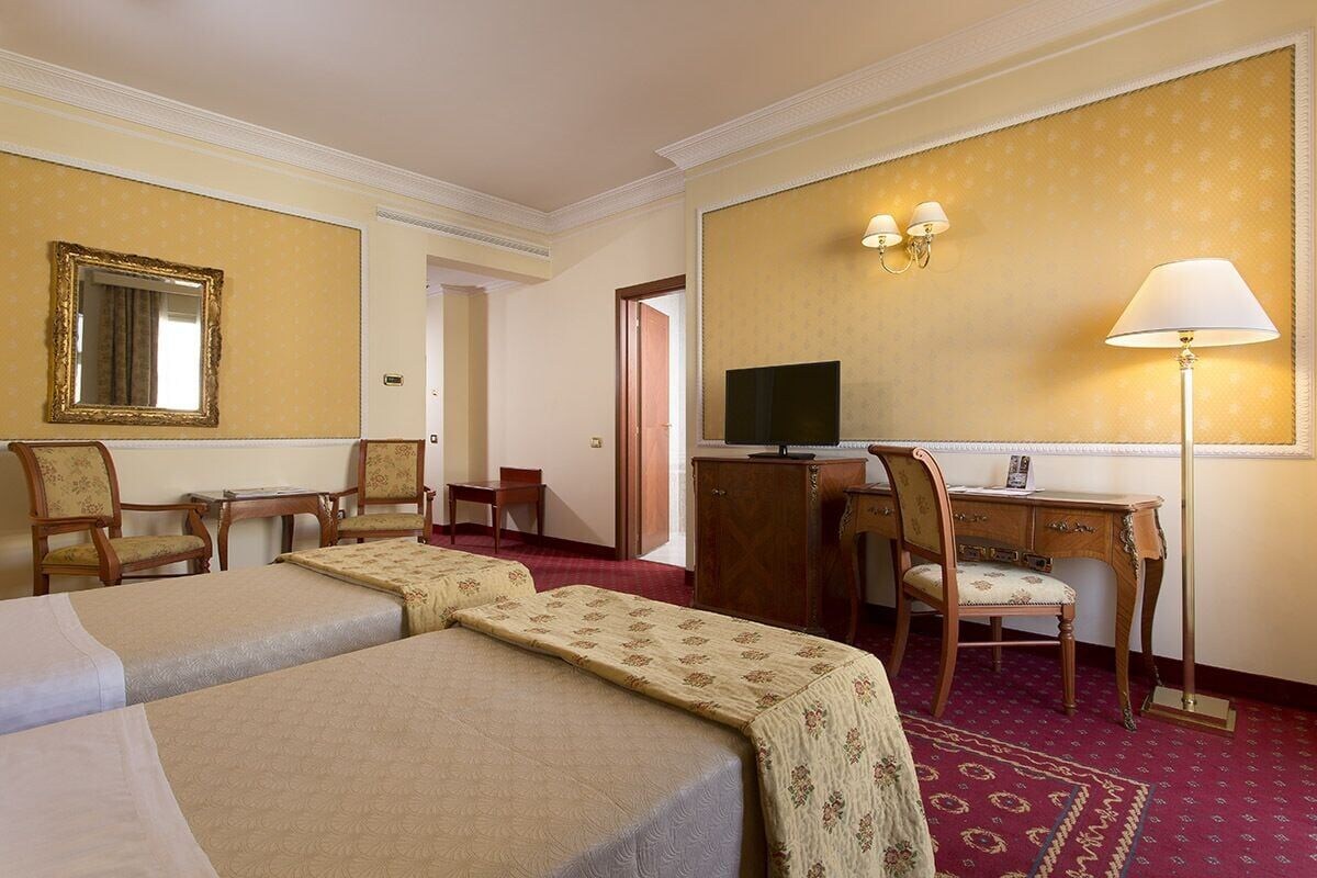 A hotel room with two beds, a desk, a chair, a television, and a lamp.