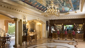 Un lobby de hotel lujoso con una gran araña, columnas ornamentadas, una zona de bar y un diseño decorativo en el suelo.