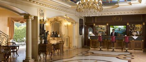 Eine luxuriöse Hotelhalle mit einem prunkvollen Kronleuchter, verzierten Säulen, einer Bar und einem dekorativen Bodenmuster.