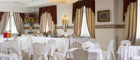 Un salón de banquetes con mesas redondas, manteles blancos y sillas.