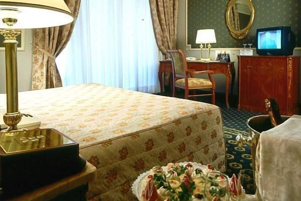 Una habitación de hotel con cama, escritorio, silla, televisor y espejo.