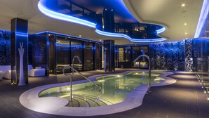 Un área de piscina interior moderna con diseño curvo, paredes de vidrio e iluminación ambiental.