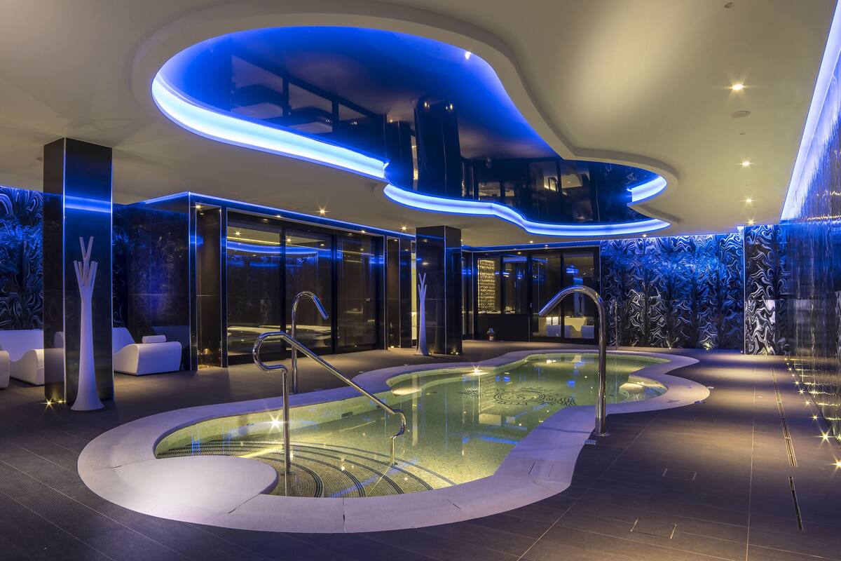 Un área de piscina interior moderna con diseño curvo, paredes de vidrio e iluminación ambiental.