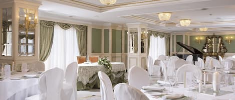 Un comedor elegante con manteles y sillas blancos, candelabros y un piano de cola.