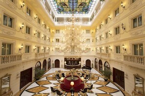 A grand hotel lobby with a central seating area, chandeliers, and a stained glass ceiling. - Grand Hotel Vanvitelli (San Marco Evangelista)