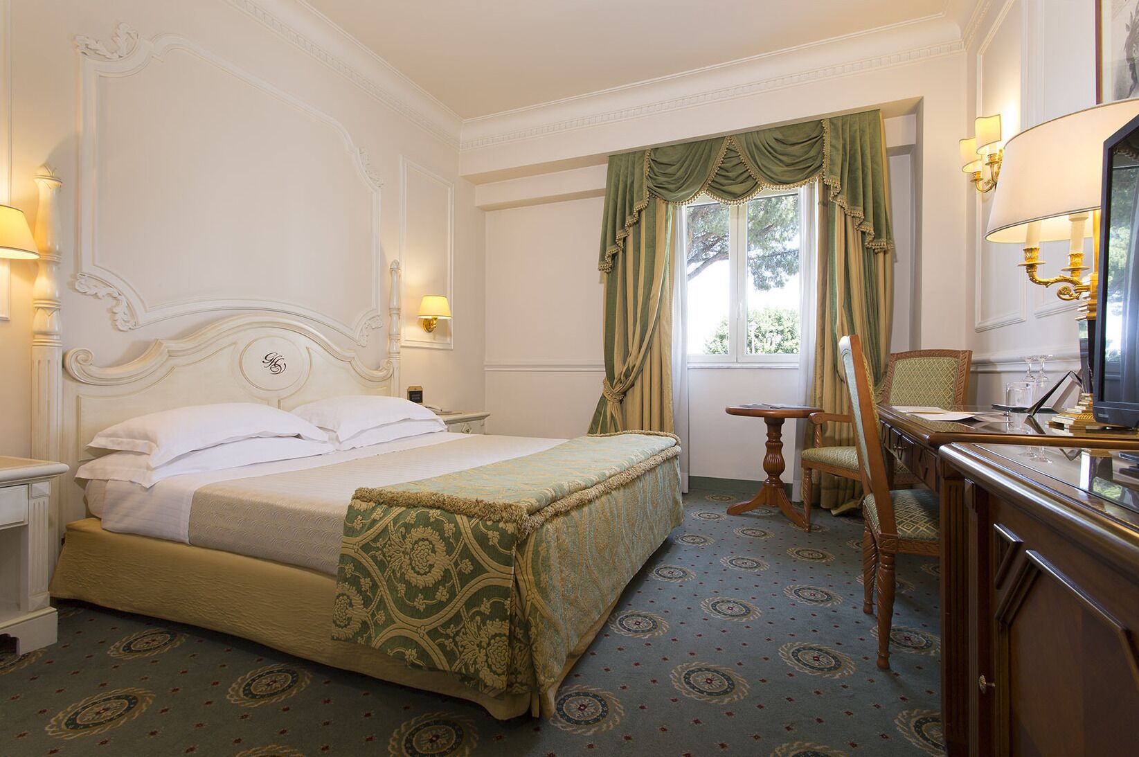 A hotel room with a large bed, a desk with a chair, a television, and a window with curtains.