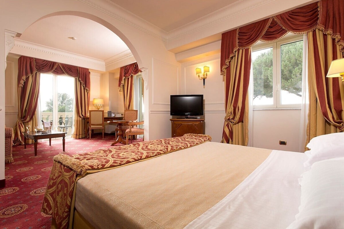Habitación de hotel con una cama grande, televisión, escritorio con silla y vistas al exterior por la ventana.