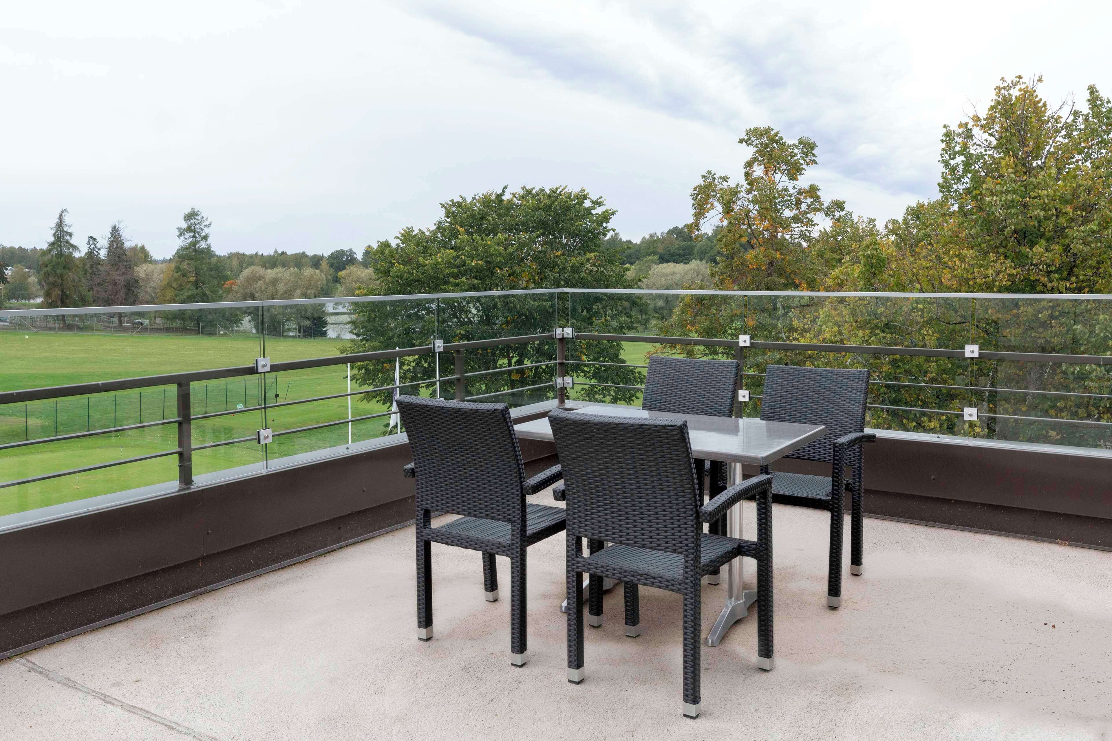 Een terras buiten met een tafel en stoelen, met uitzicht op een groen veld en bomen.