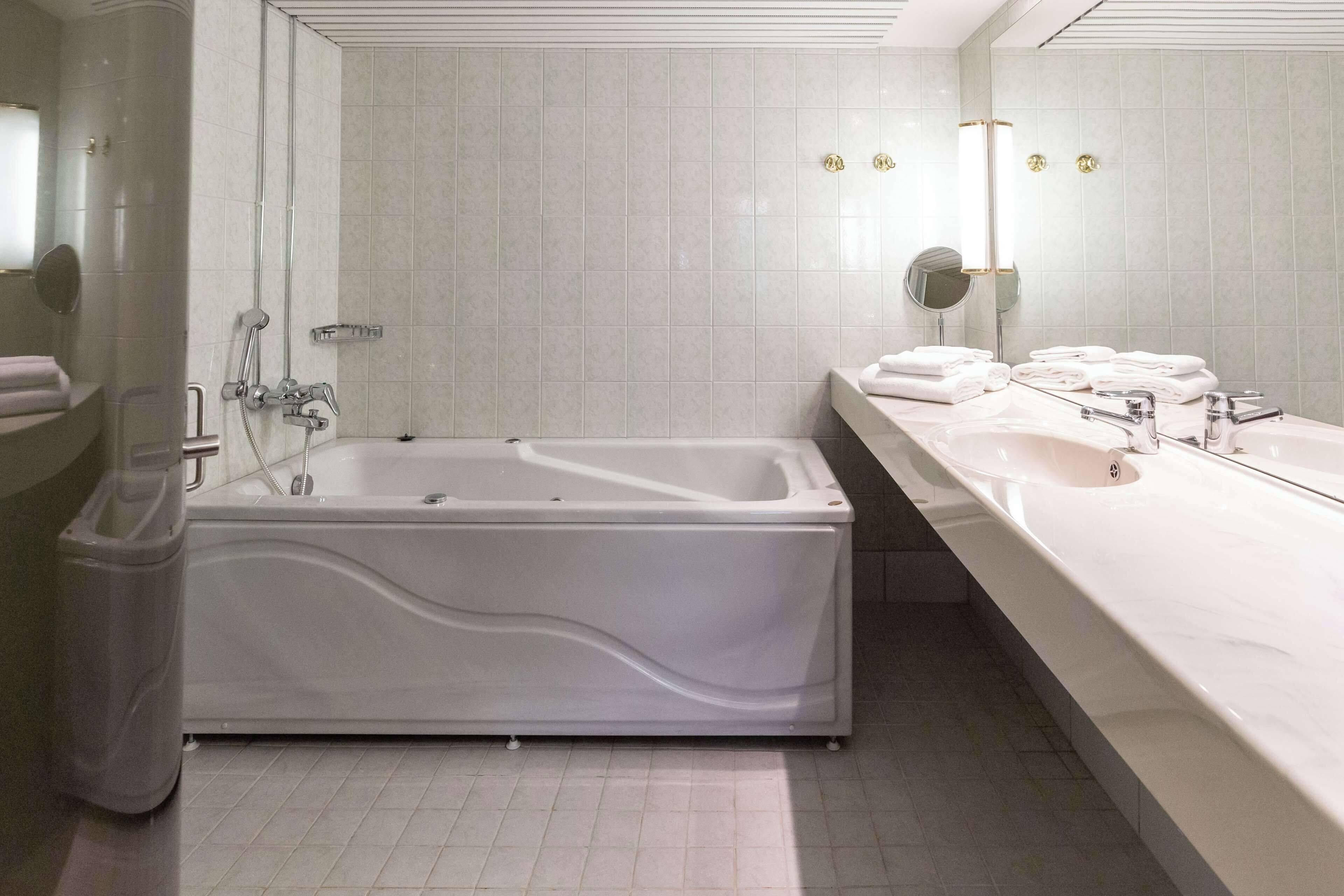 Une salle de bain moderne avec une grande baignoire, un long meuble-lavabo doté de plusieurs vasques et un grand miroir.