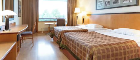 A hotel room with two beds, a desk, a chair, a window with curtains, and a framed picture on the wall.