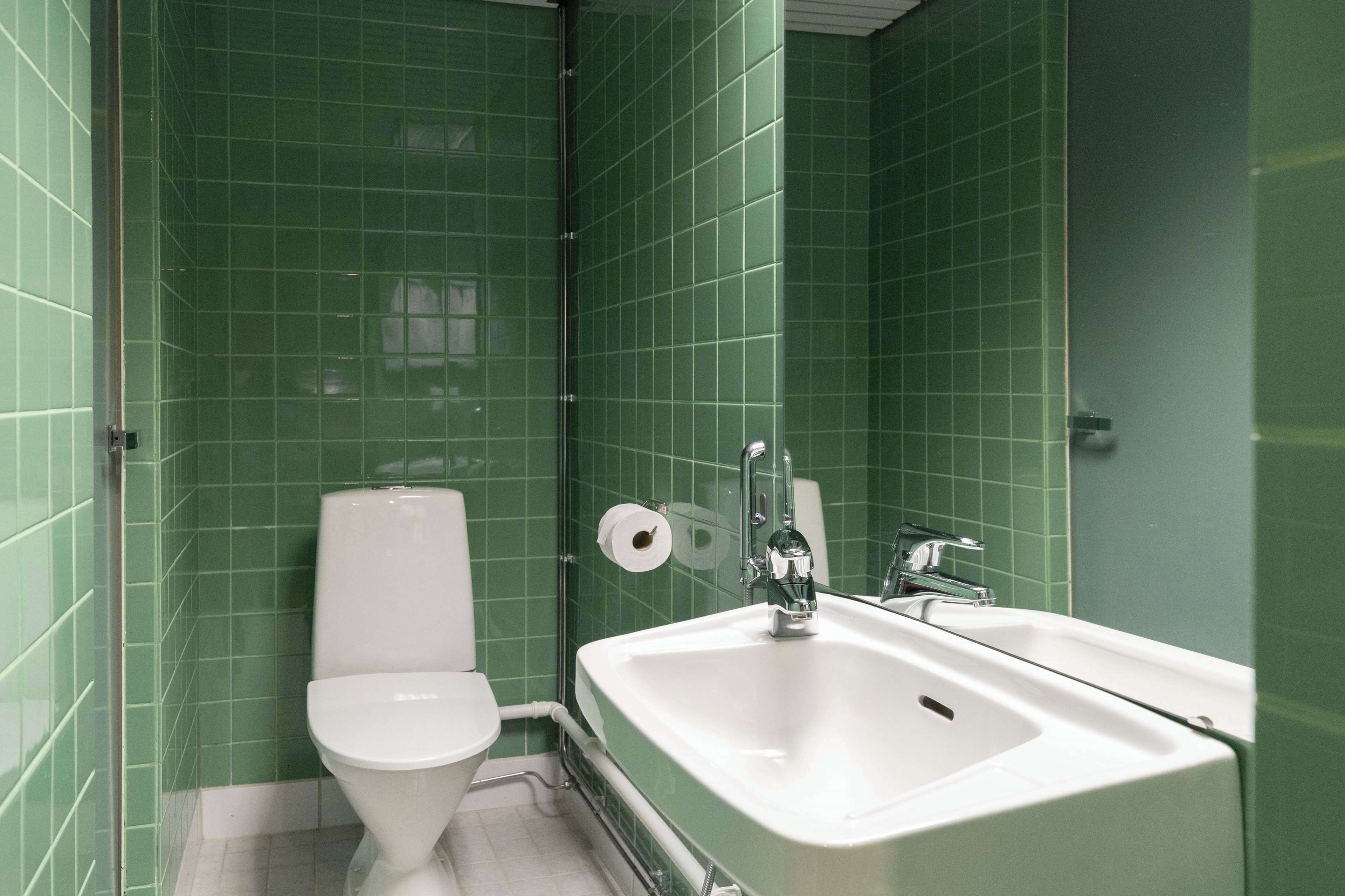 A bathroom with green tiled walls, a white toilet, and a white sink with a mirror.