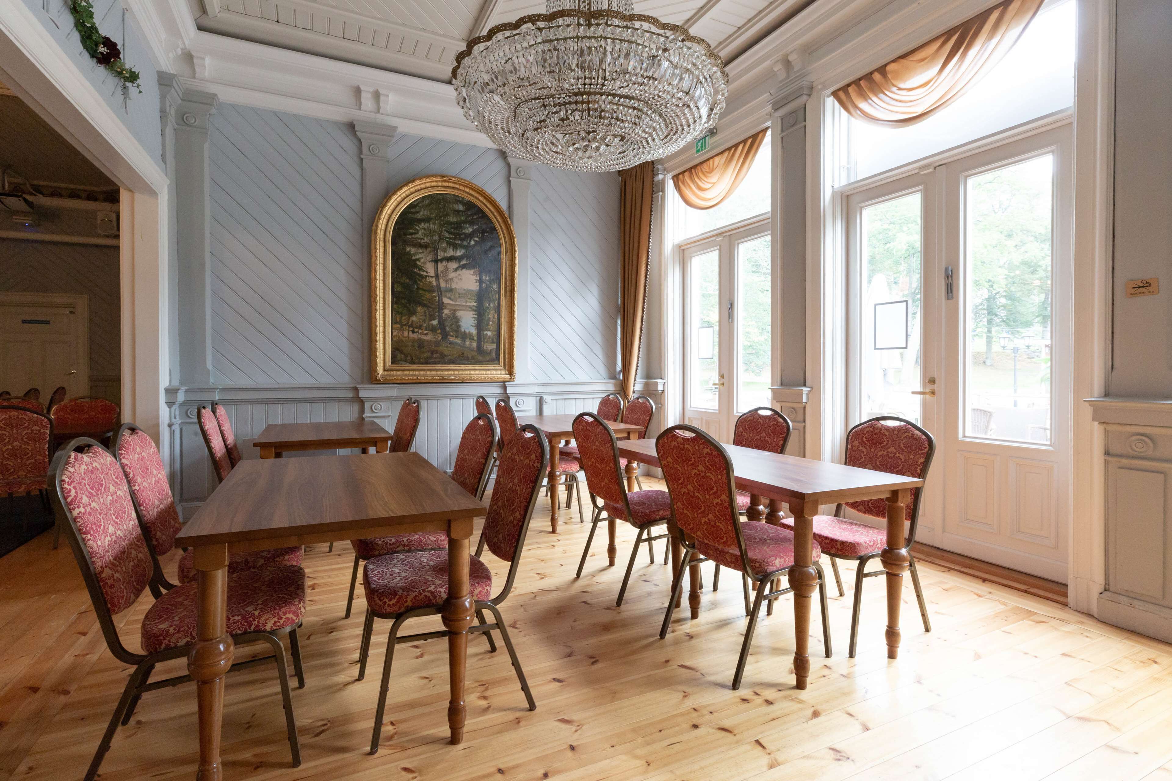 Une salle à manger avec une grande table en bois et des chaises à revêtement rouge, un lustre et un grand tableau encadré au mur.