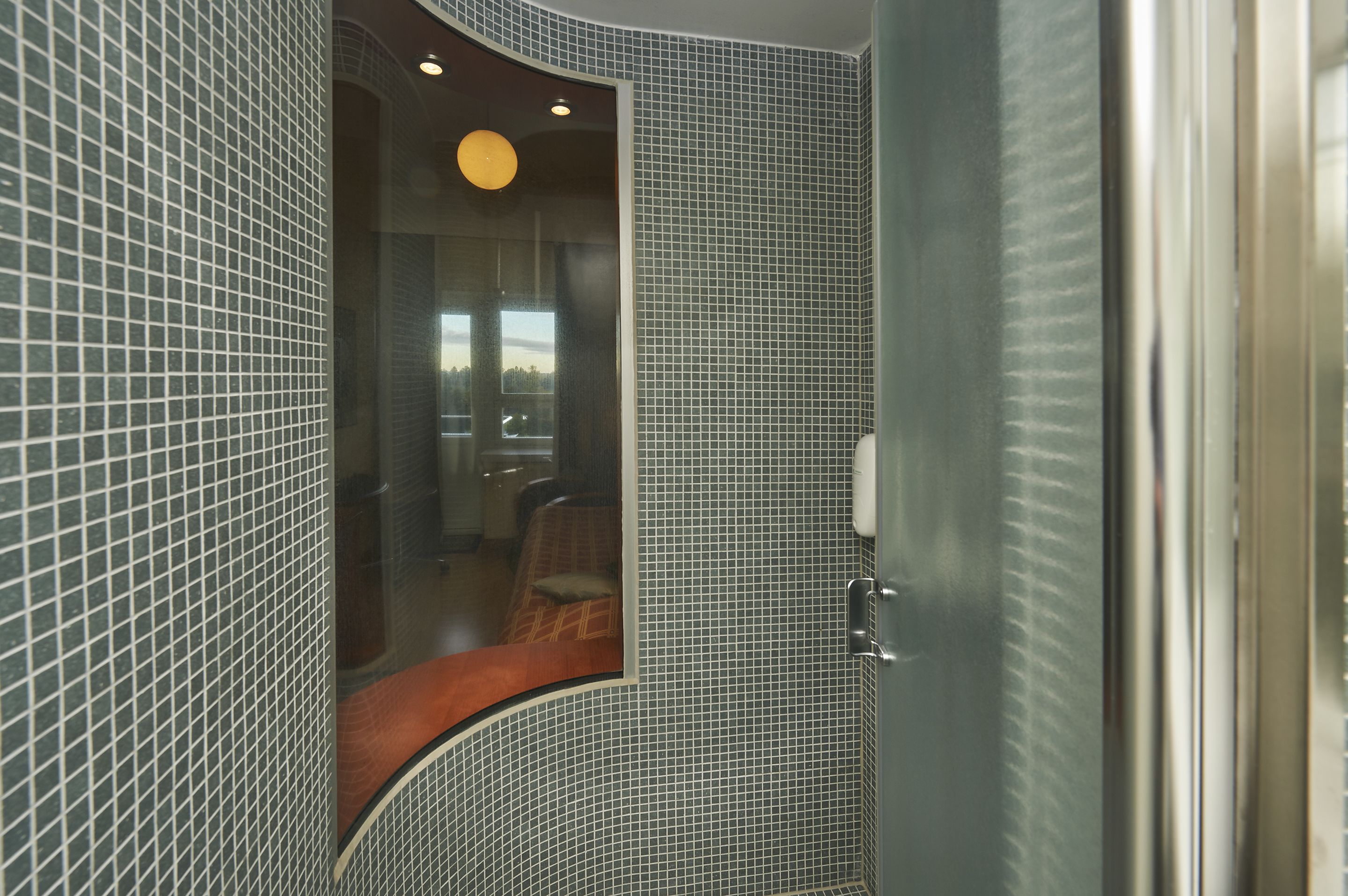 Une salle de bain avec un miroir incurvé, des murs carrelés et un espace douche bien délimité.