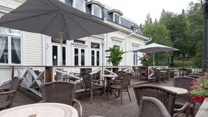 A deck with wicker chairs and tables, umbrellas, and a building with a sign reading "KESAKAHVILA". - Scandic Aulanko (Hameenlinna)