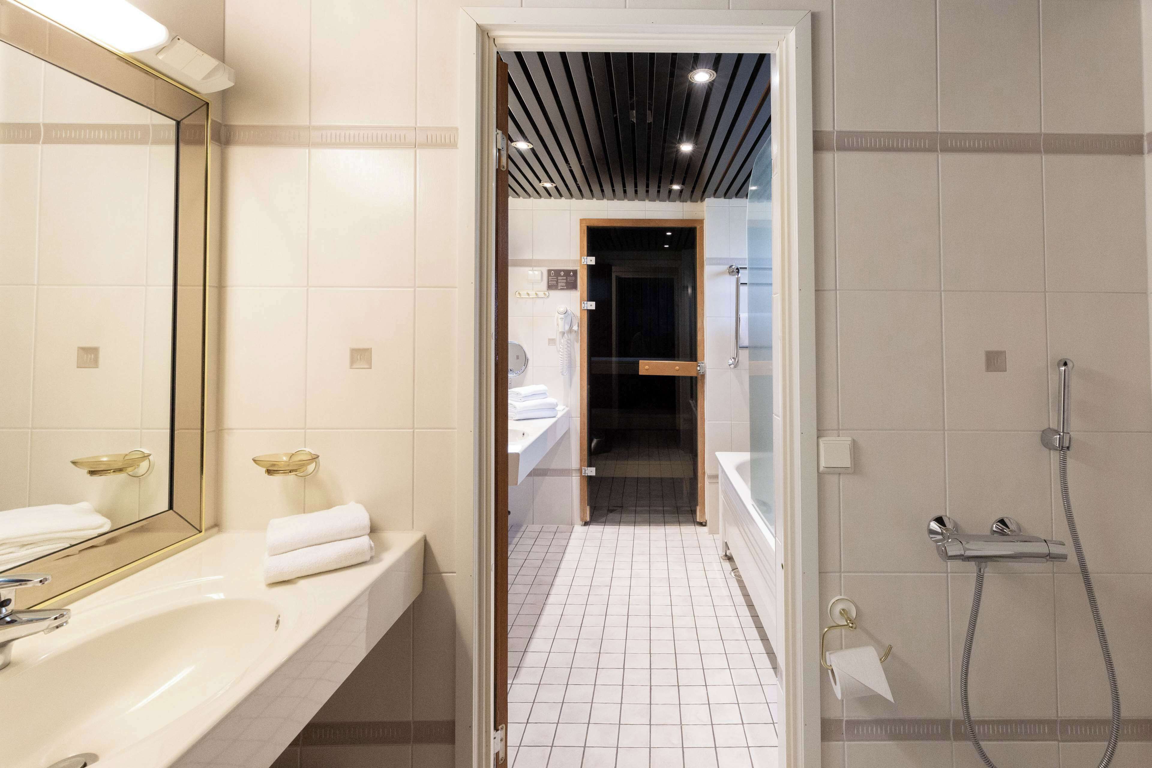 Ein modernes Badezimmer mit großem Spiegel, weißem Waschbecken und Duschbereich.