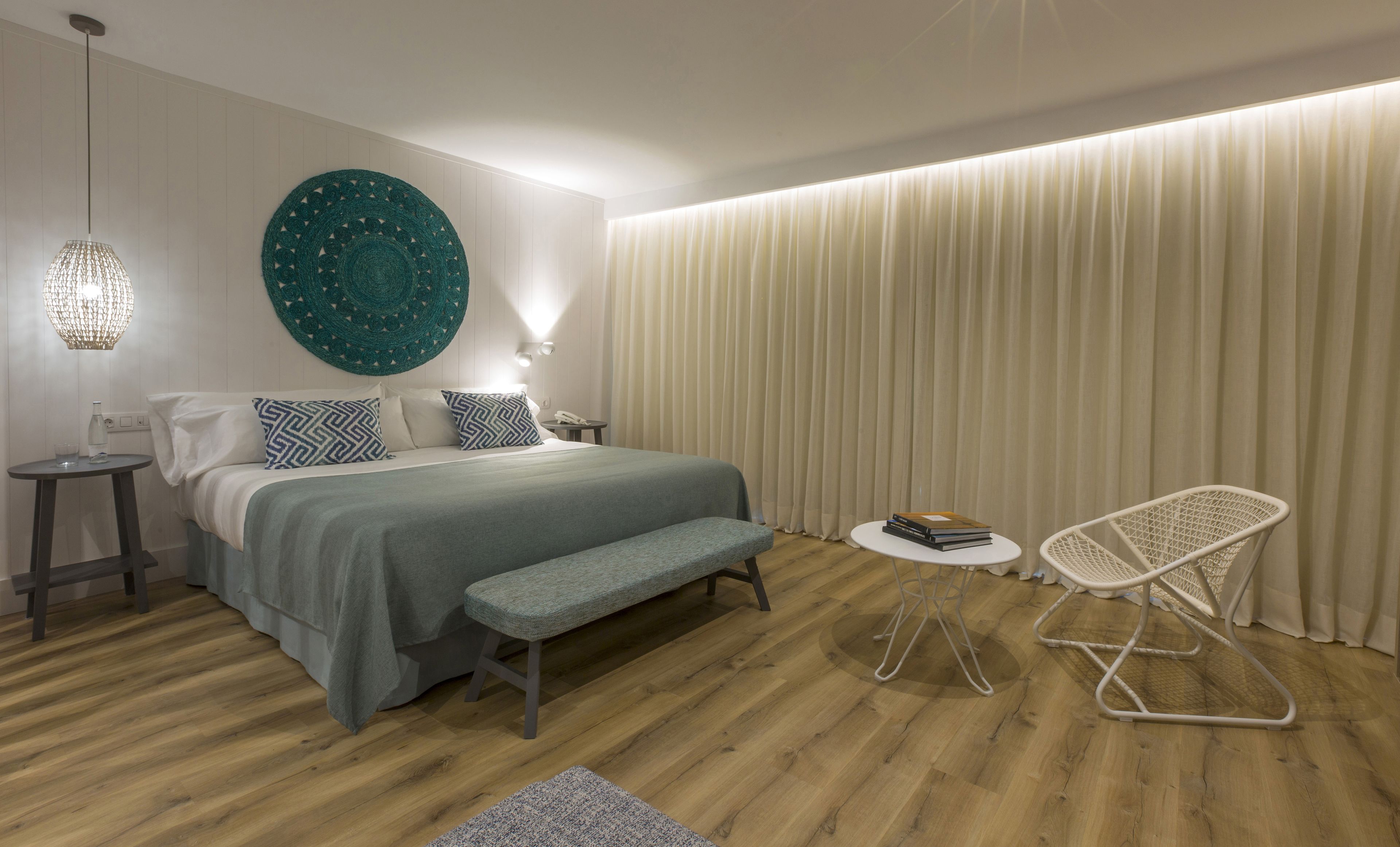 Ein modernes Schlafzimmer mit einem großen Bett, Nachttischen, einer Bank, einem Stuhl und einer runden Wanddekoration.