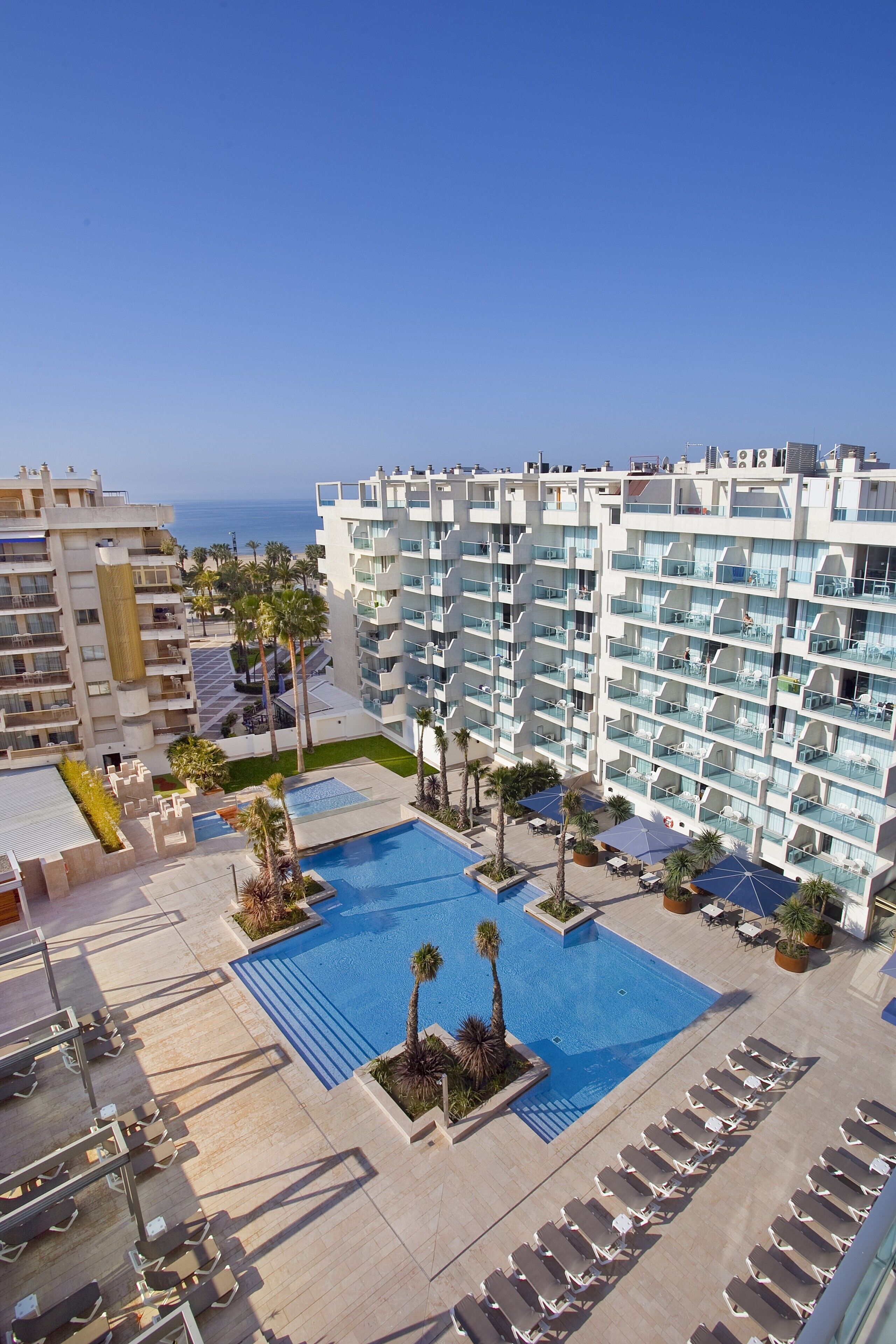 Un resort con una piscina grande, tumbonas y vistas al océano.