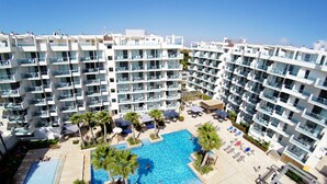 A large pool surrounded by palm trees and lounge chairs, with a modern apartment building in the background. - Blaumar Hotel Salou (Salou)