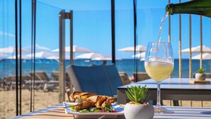 A table with a glass of white wine, a plate of grilled chicken, and a small potted plant. - Blaumar Hotel Salou (Salou)