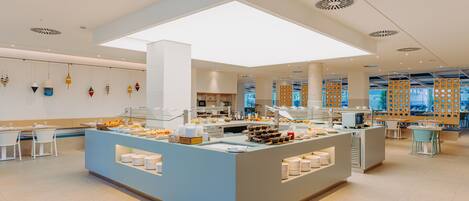 A modern breakfast area with a central counter, seating, and a view of the city through large windows.