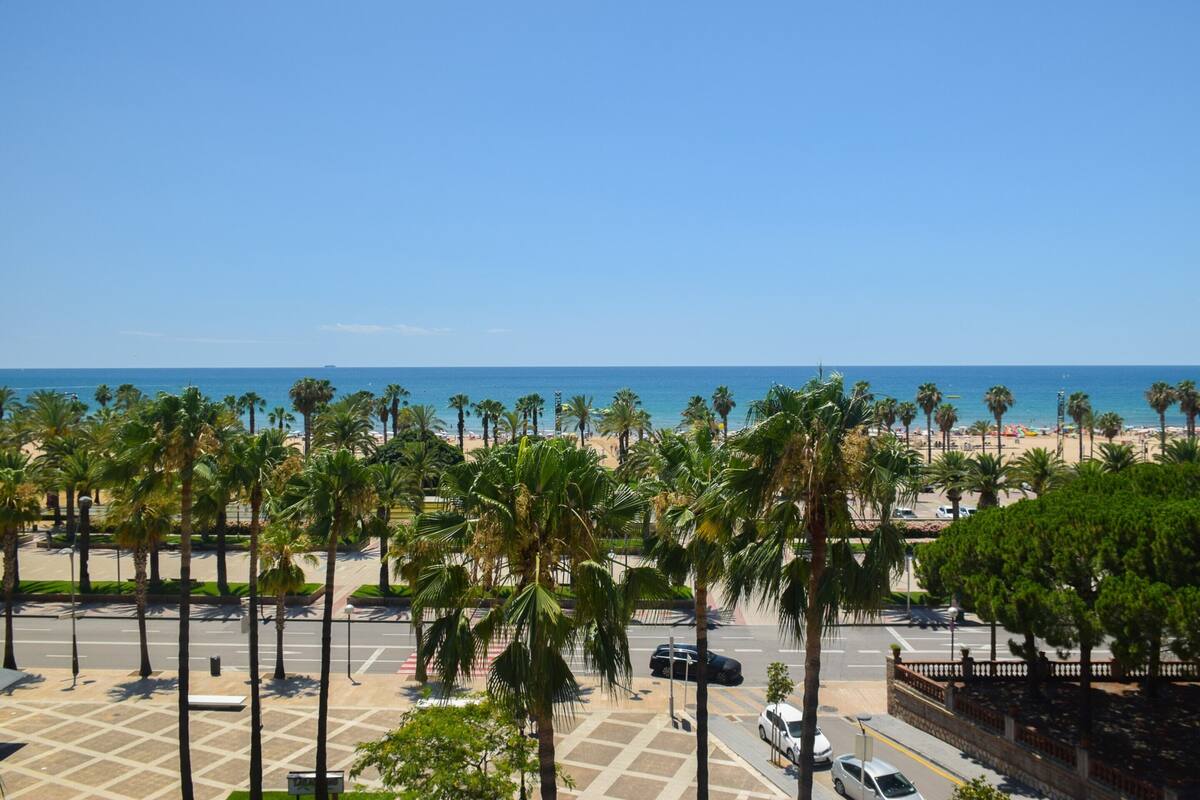 A coastal view with palm trees, a beach, and a clear sky.