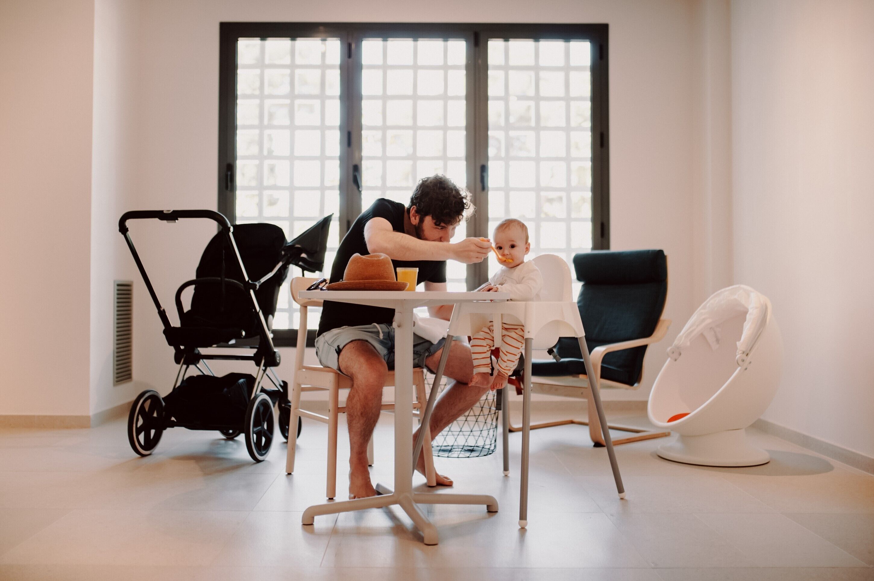 A room with a dining table, a baby high chair, a stroller, and a rocking chair.