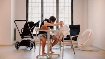 A room with a dining table, a baby high chair, a stroller, and a rocking chair.