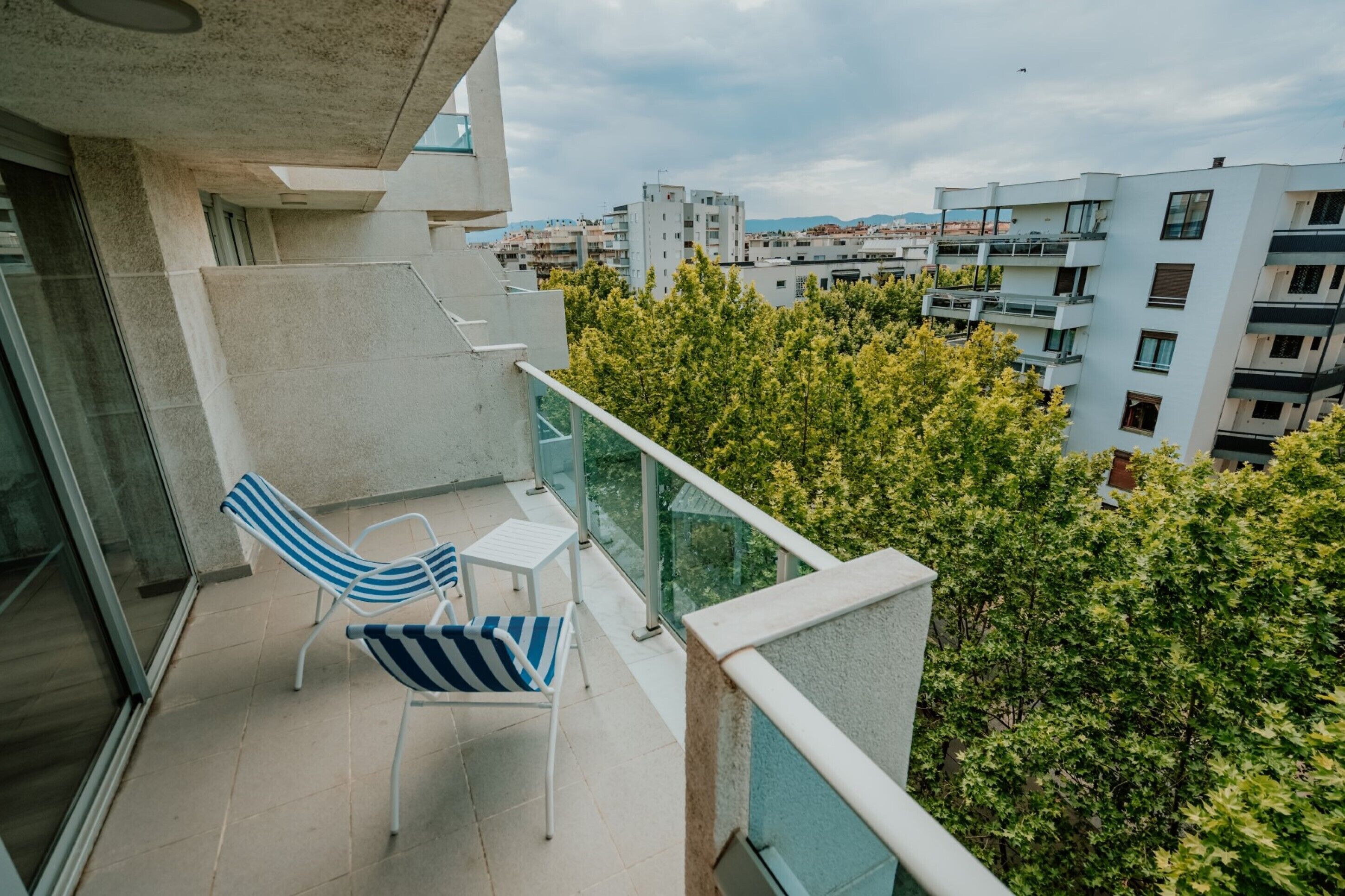 A balcony with a glass railing, a chair, and a small table.